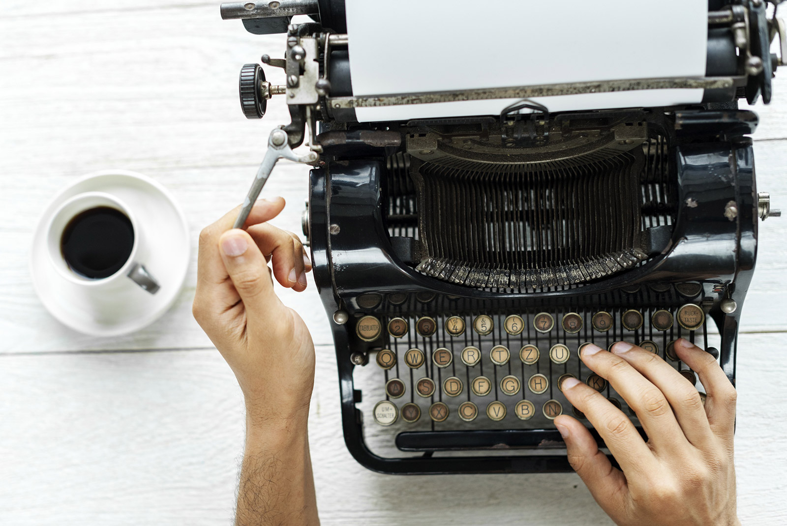 Person using typewriter with a cup of coffee to the side